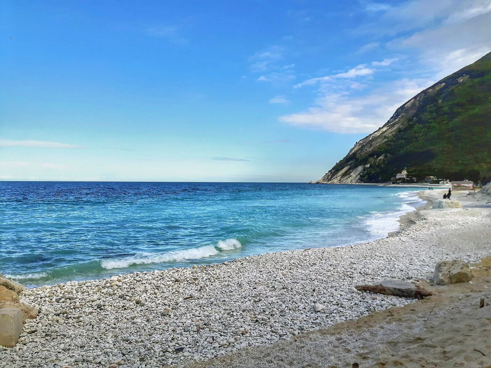 Spiaggia di ciottoli bianchi a Portonovo con il mare turchese e il Monte Conero ricoperto di bosco sullo sfondo